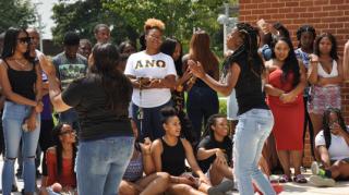 Diverse group of students standing outside watching a performance of students wearing black tshirts and jeans.