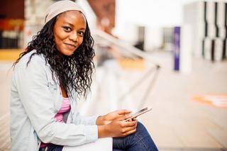 Photo of young student using smartphone and sitting in front of university