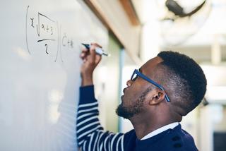 Male student writing on a whiteboard in a classroom